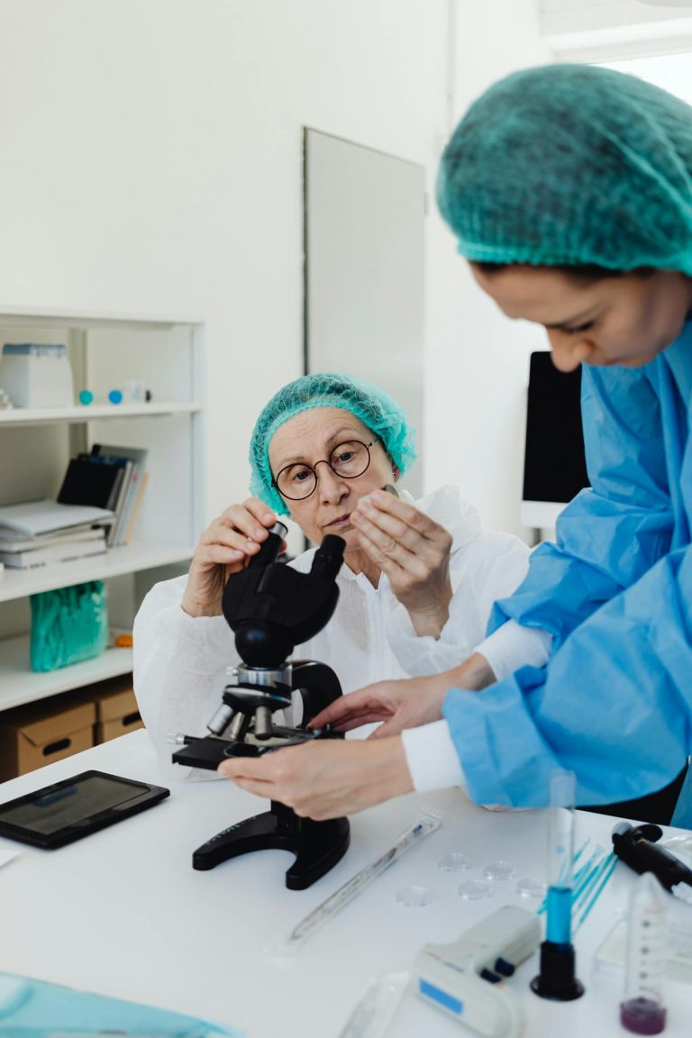 Researchers using microscope in a medical lab setting, equipped with protective gear and scientific tools.