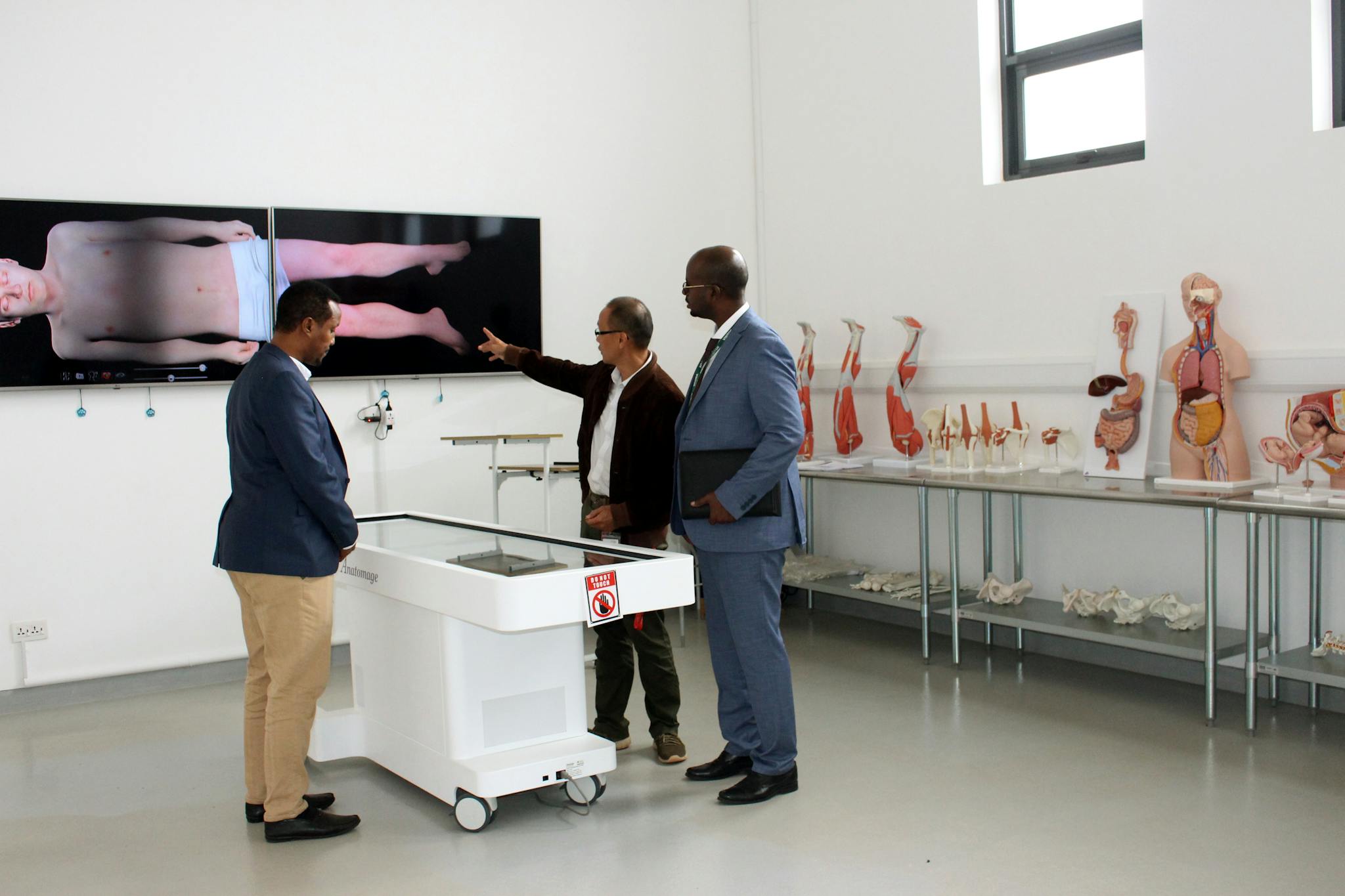 Three professionals discussing anatomy in a modern laboratory environment.