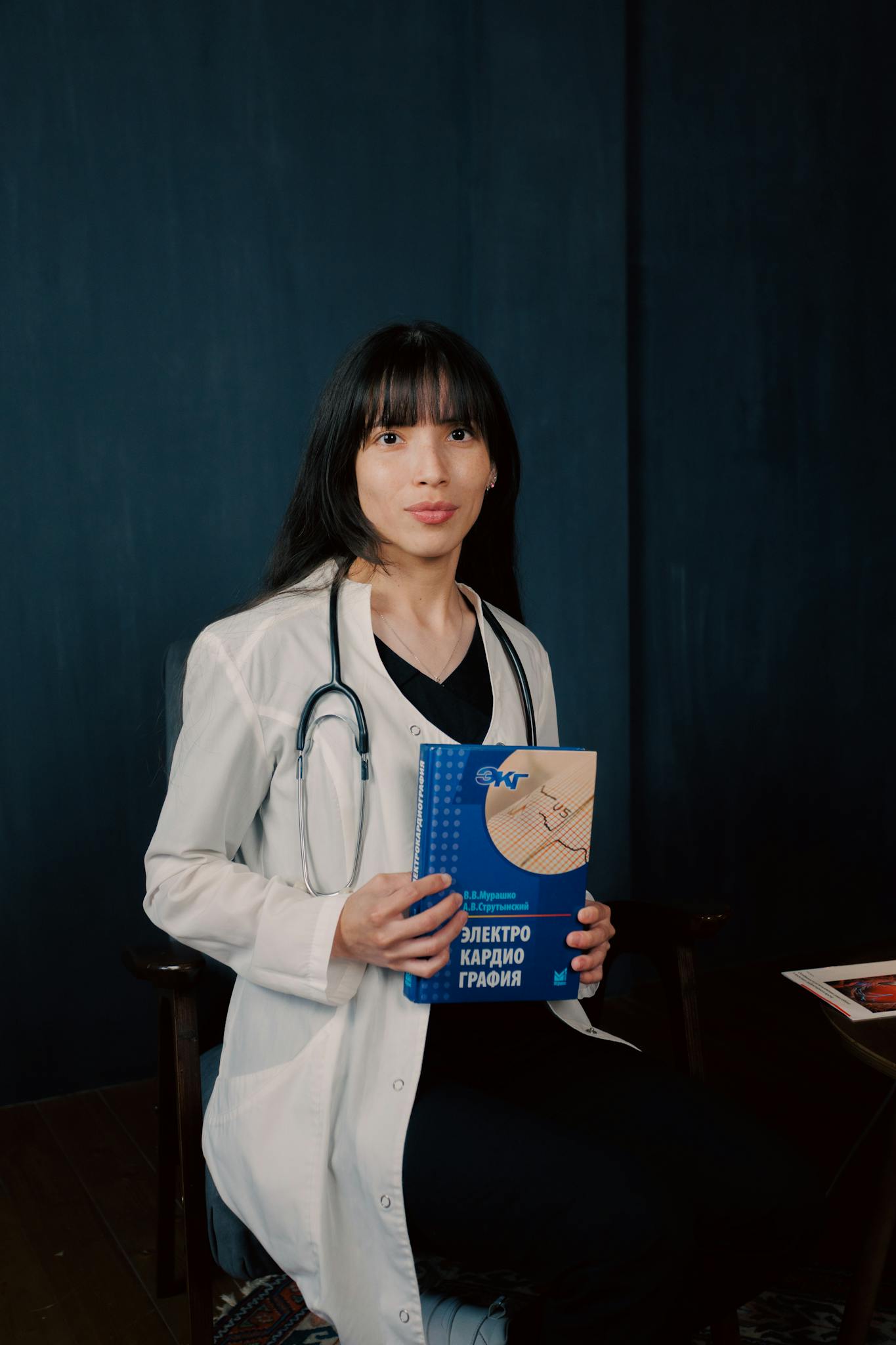 Young female doctor in lab coat with stethoscope, holding a book on electrocardiography.